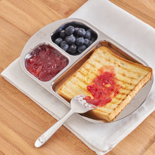 Load image into Gallery viewer, Shiny stainless steel baby divided plate that fits  one whole toast and couple of side dishes. The food pusher or butter speader is used to spread strawberry jam.
