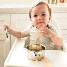 Load image into Gallery viewer, A baby is holding a Kiddobloom baby safe fork made of stainless steel 304 from a stainless steel bowl with handles on the side. 
